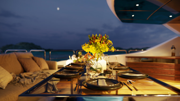 Visualization of a glass table on a luxury yacht positioned on the rear cockpit with a close-up on the plates, wine glasses and cutlery with flower bouquet and candles in the background